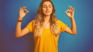 Junges Mädchen mit langen Haaren steh mit geschlossenen Augen und gehobenen Armen, während sie beidseitig das Gyan Mudra mit ihren Händen macht