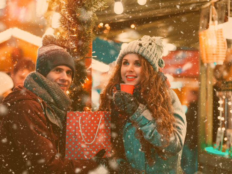 Junges Paar steht gemeinsam auf dem Weihnachtsmarkt und wärmt sich an ihren wohlig waren Getränken in ihren Händen