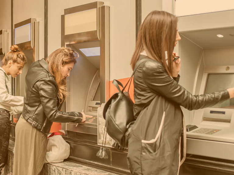 Vier Mädchen stehen vor je einem Geldautomaten