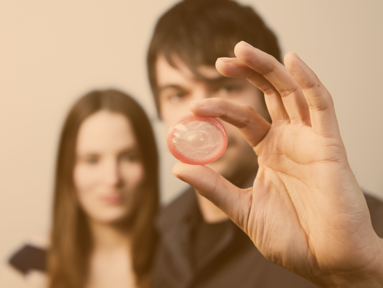 Teenager-Paar, er im Vordergrund hält ein Kondom ins Bild