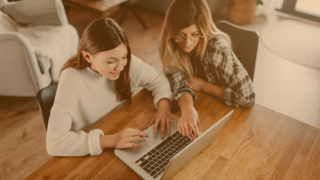 Mutter und Tochter sitzen am Tisch und machen am Laptop Schulaufgaben