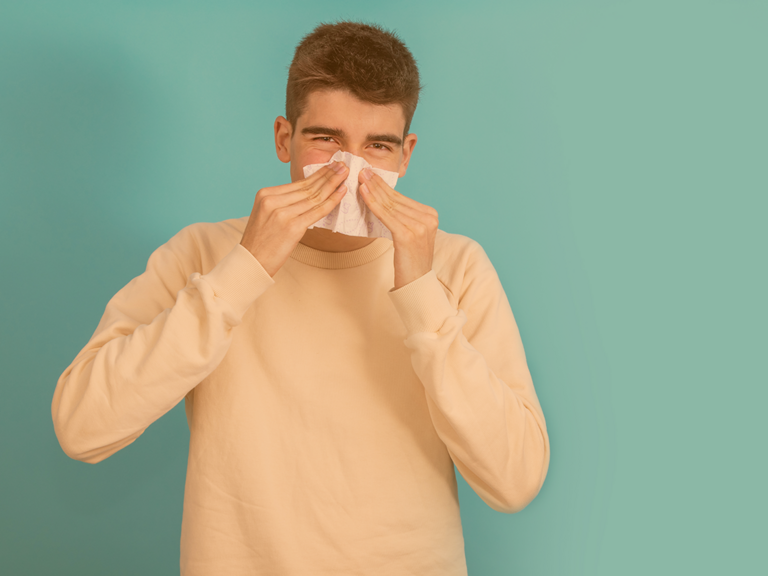 Dunkelhaariger Teenager schnäuzt sich die Nase vor farbigem Hintergrund